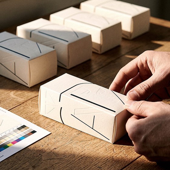 Gloved hands closing the lid of a finished presentation box, three identical boxes behind