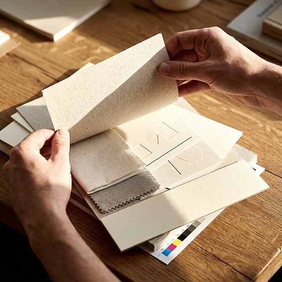 Hands turning the page of an open brand standards booklet beside paper and fabric swatches